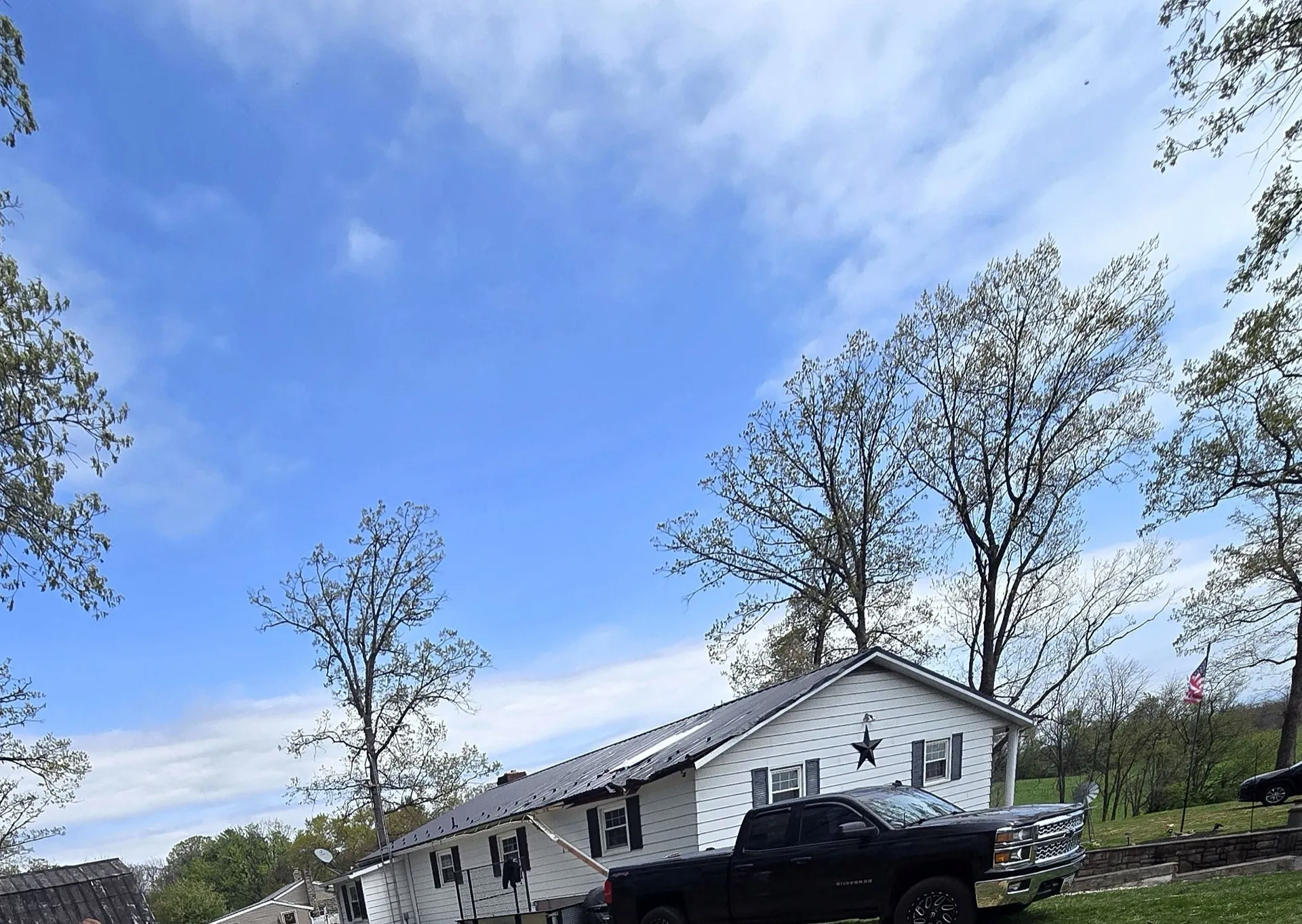 Rural Pennsylvania home with mature trees, a metal roof, and an American flag on the front lawn.